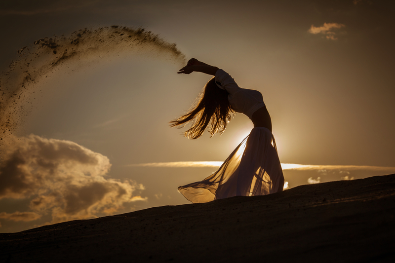 A woman (an eclectic witch) in a flowing dress dances freely at sunset; energy (magick) streams (is cast) from her hand.