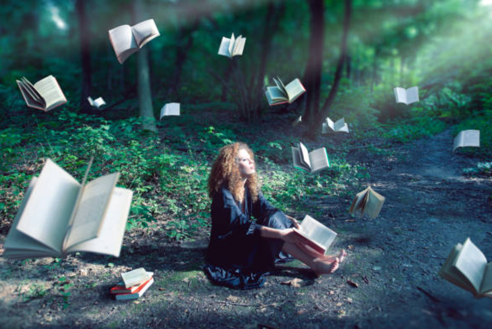 Photo of a woman (a witch) sitting in the forest with many books swirling around her, indicating that she has many choices about what she can learn about Witchcraft.