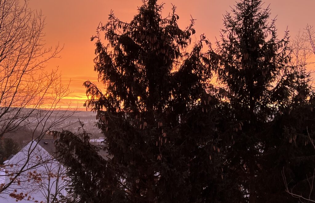 Winter sunrise seen from magick room window, snow-covered mountains glowing in morning light.